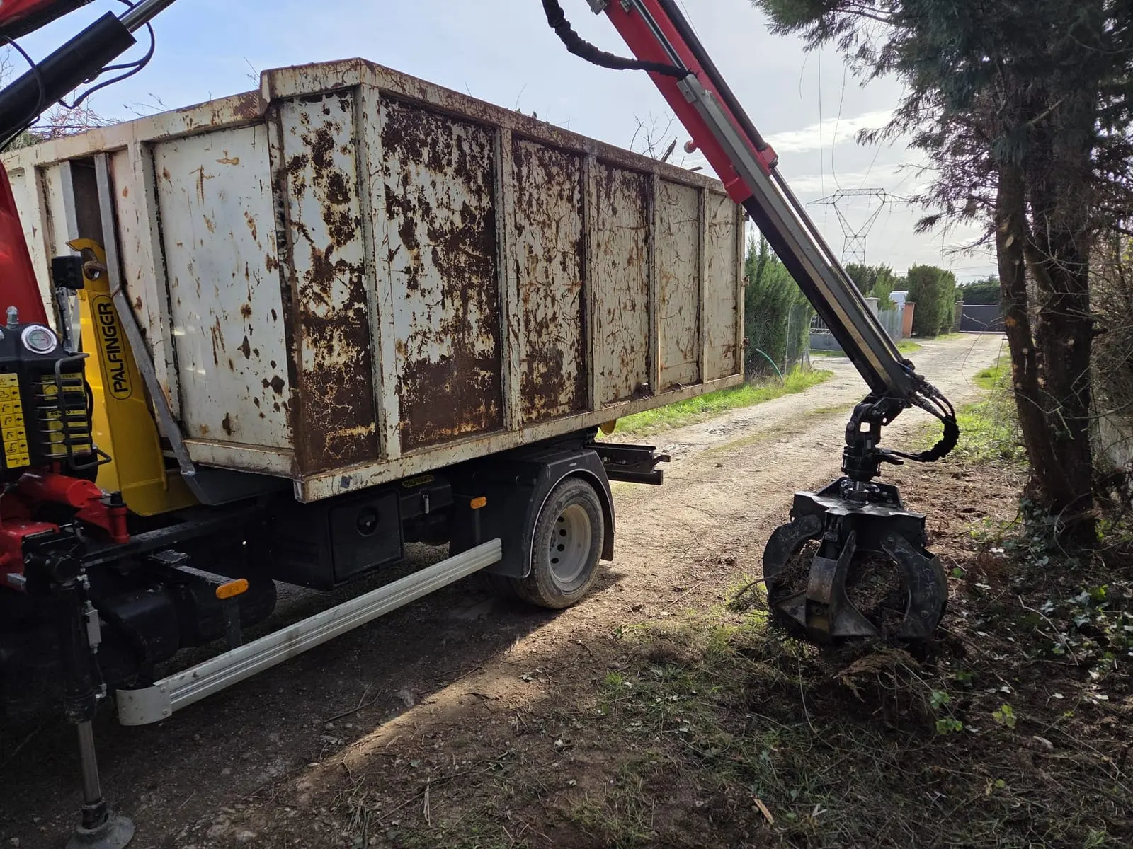 Grappin du camion de l’Entreprise Perrin au-dessus de la benne, sur un chemin de campagne